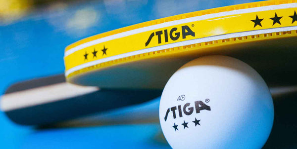 a stiga yellow ping pong paddle resting on top of a stiga 3 star ping pong ball